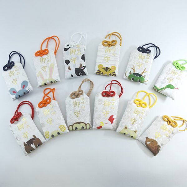 A collection of twelve colorful omamori charms, each featuring a different animal from the Japanese zodiac. The charms are arranged in a row against a simple background.