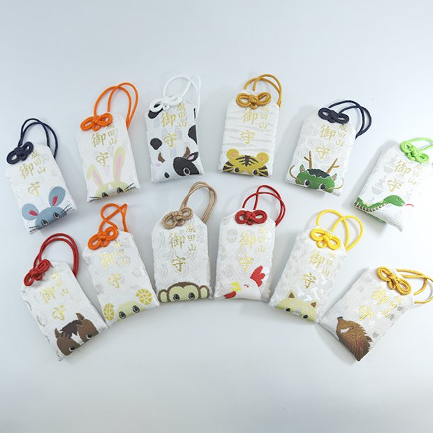 A collection of twelve colorful omamori charms, each featuring a different animal from the Japanese zodiac. The charms are arranged in a row against a simple background.