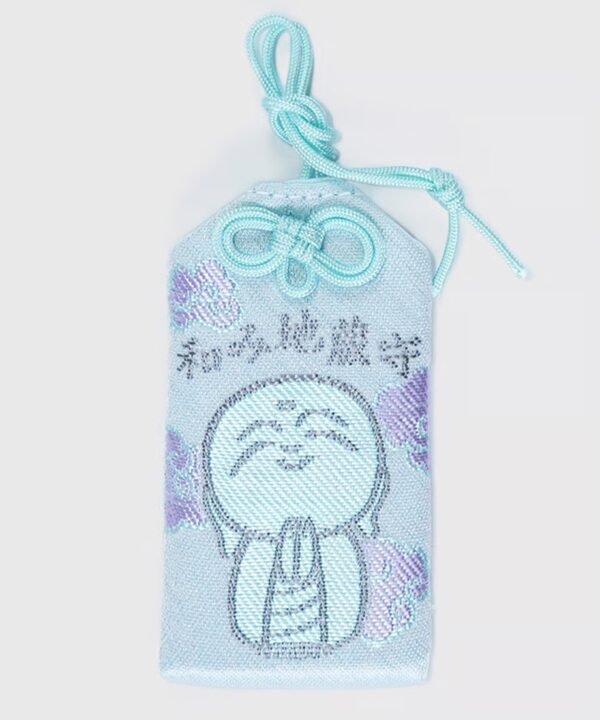 Light blue Japanese omamori with a black embroidered Jizō Bodhisattva figure and purple flowers.