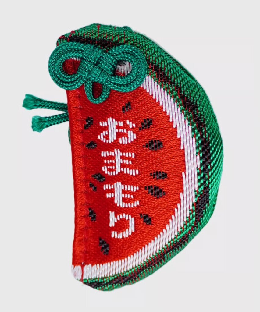 Watermelon-shaped omamori with red flesh, black seeds, and a green rind, featuring the white embroidered text "Omamori" in Japanese.