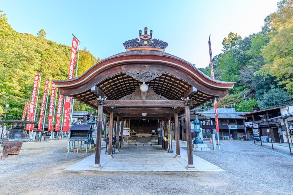 Ornate wooden worship pavilion with a curving roof, surrounded by red banners and the green backdrop of the forested hills.